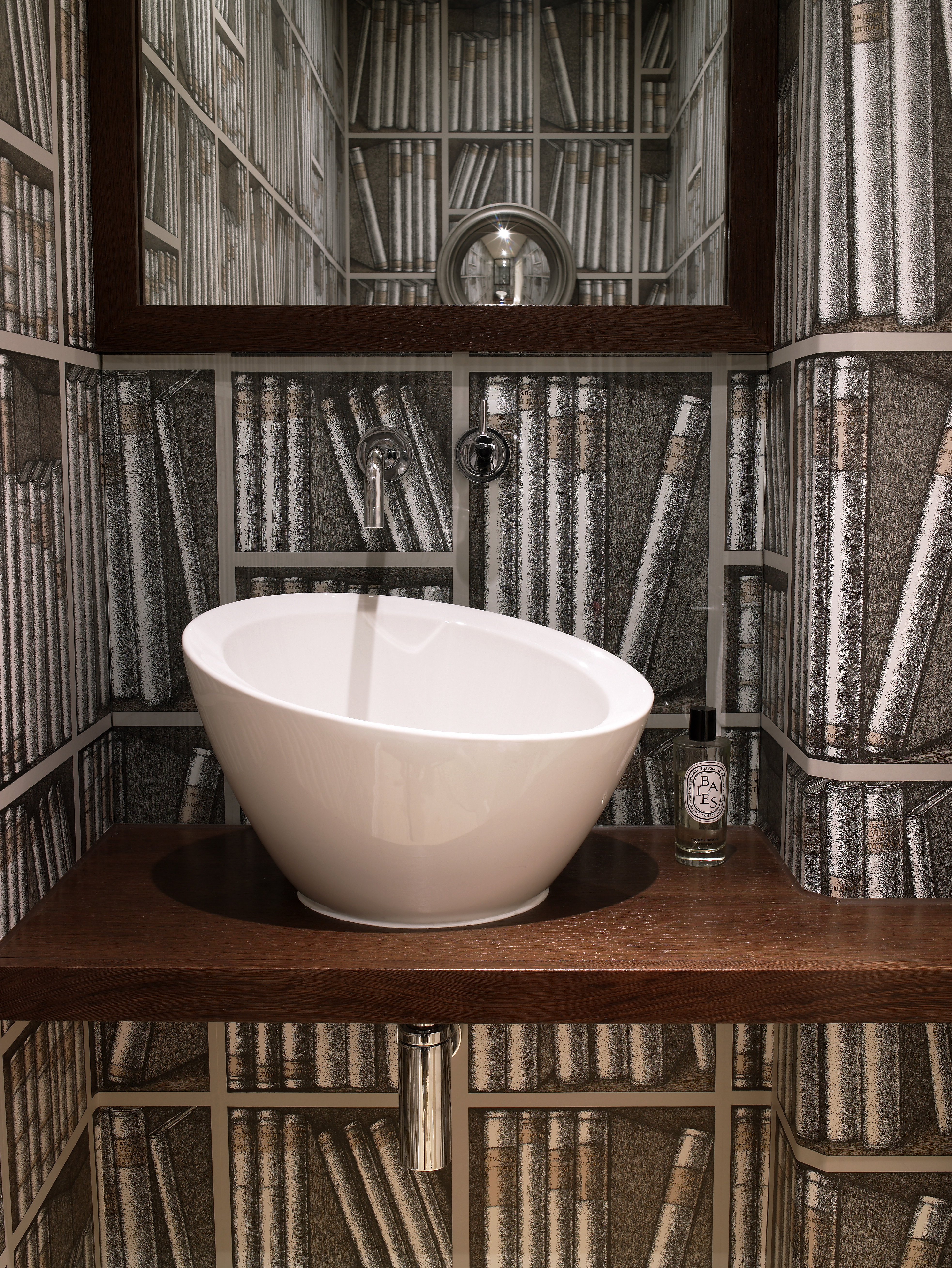 Cloakroom with ebonised wooden shelf and contemporary basin and Cole & Son bookshelf wallpaper.