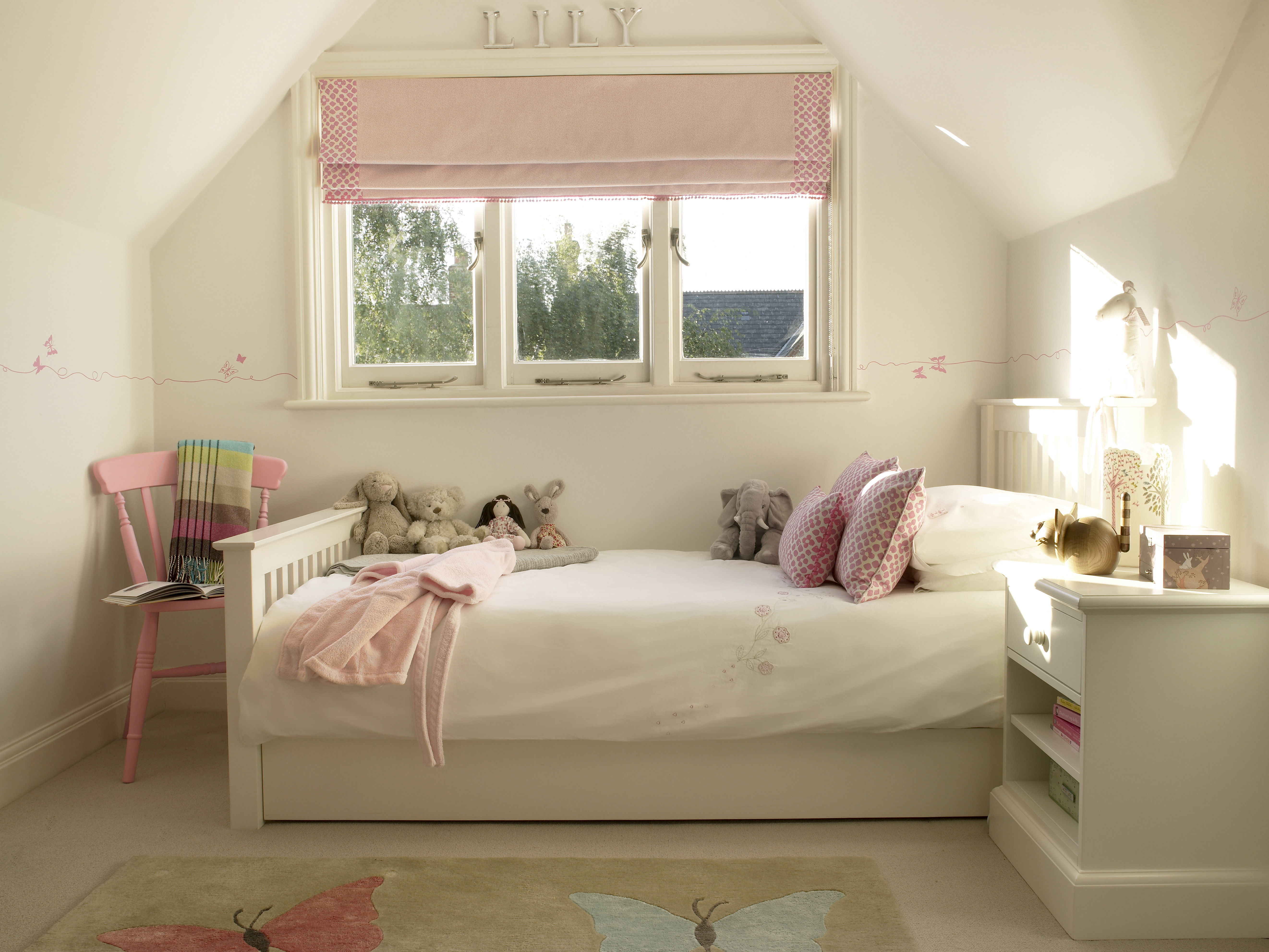 Girls white bedroom with pink butterfly stencils and contemporary pink roman blind with pompom trim.