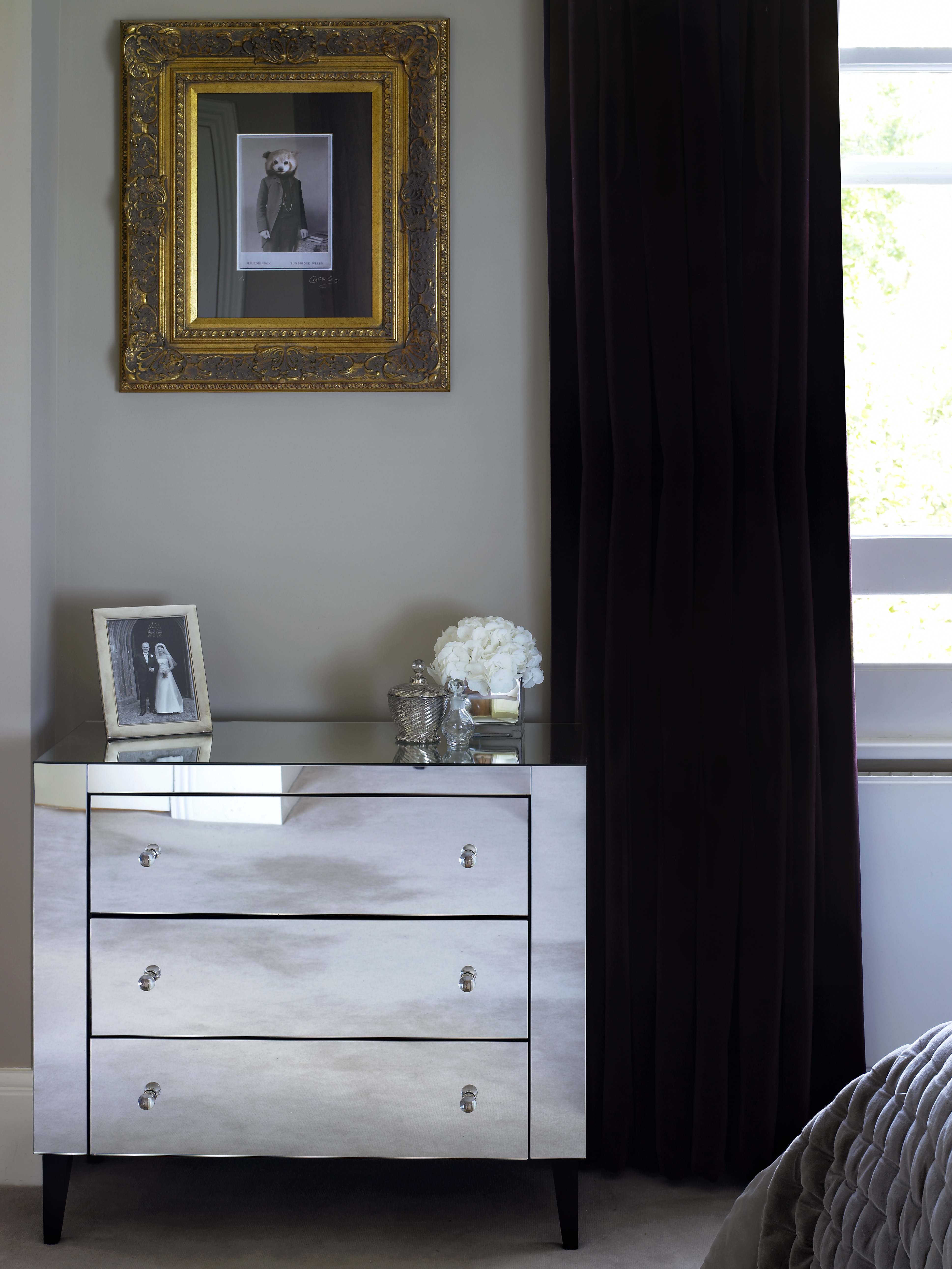 Close up of upholstered headboard and bed cushions alongside smoked glass pebble lamps by Porta Roman, reflected in mirror on walnut wardrobes.