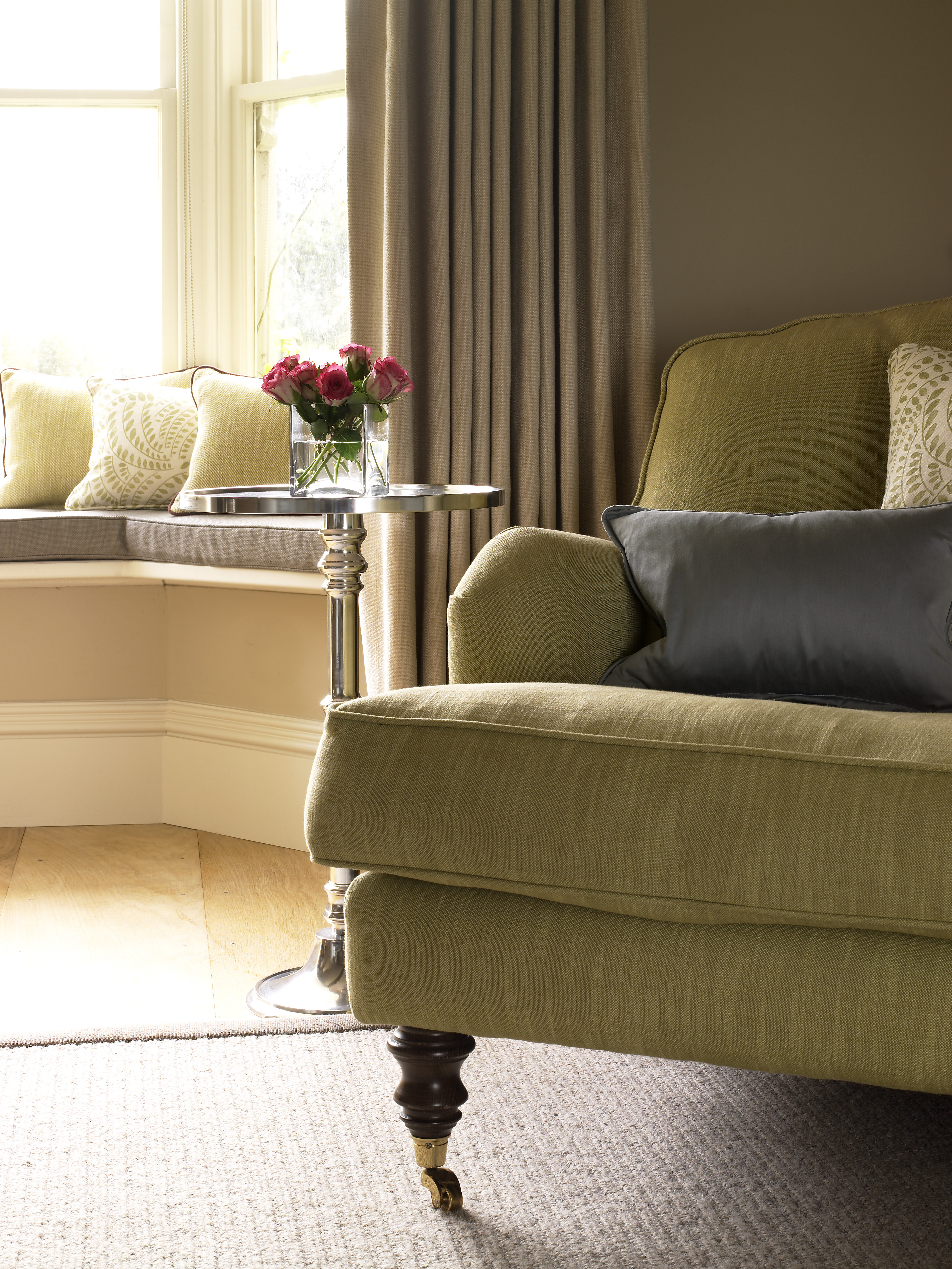 Close up of armchair and cushions with side table in timeless design scheme, showing bay window seating area.