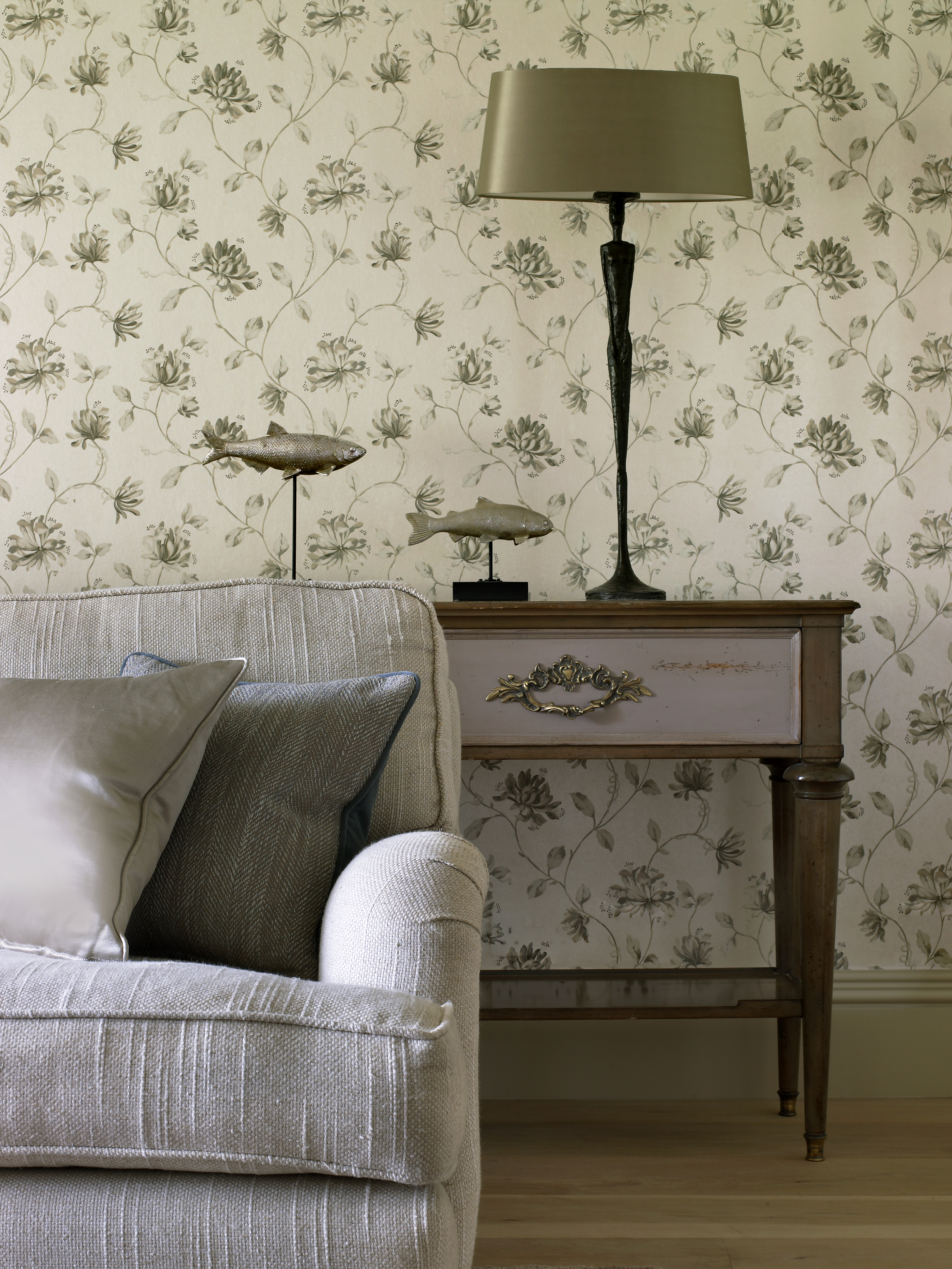 Armchair and cushions to the front of classic styled console and bronzed sculpted table lamp by Porta Romana.
