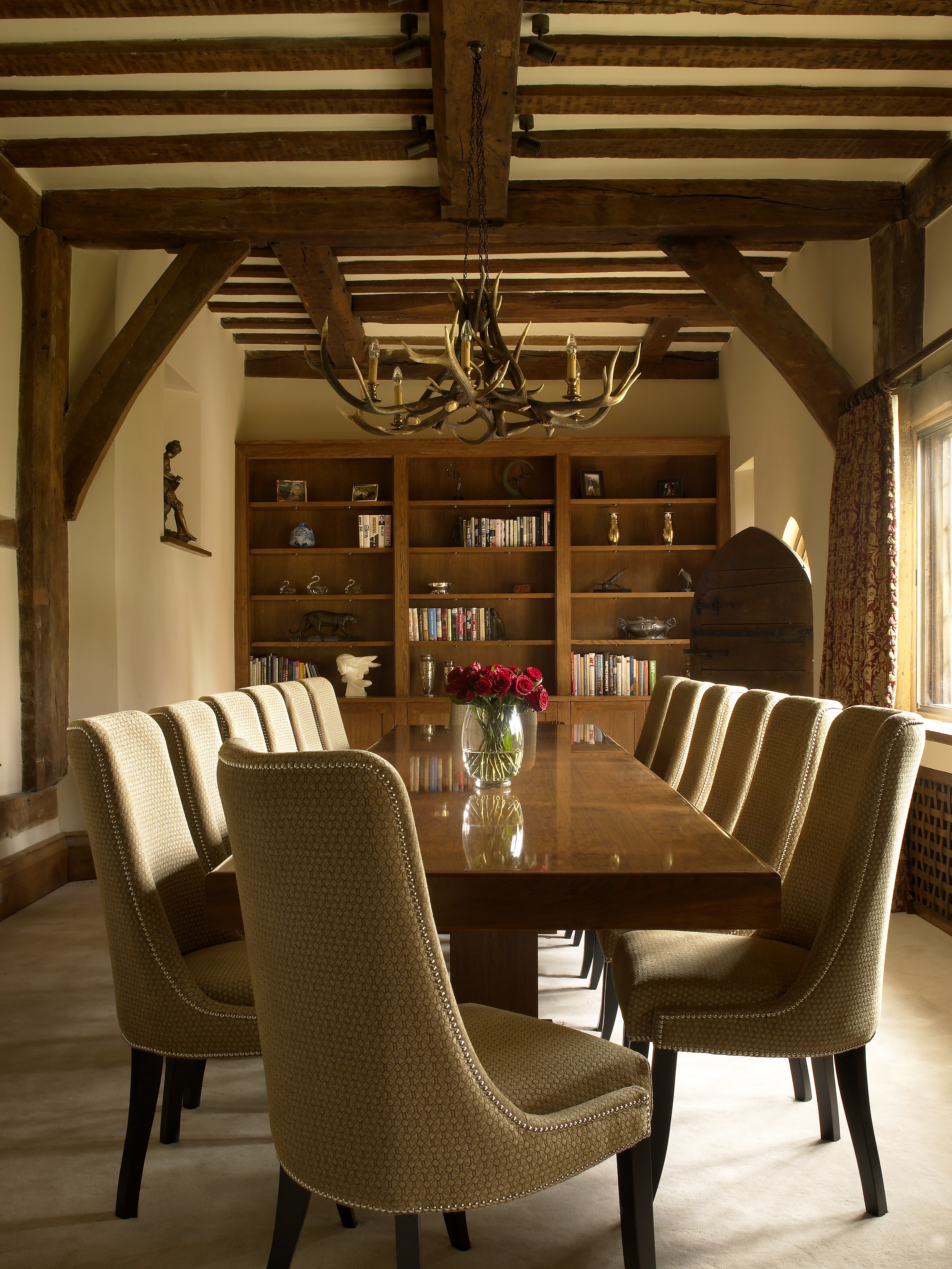 Classical styled dining room with original oak beams, polished wood dining table with upholstered and studded dining chairs and antler chandelier.