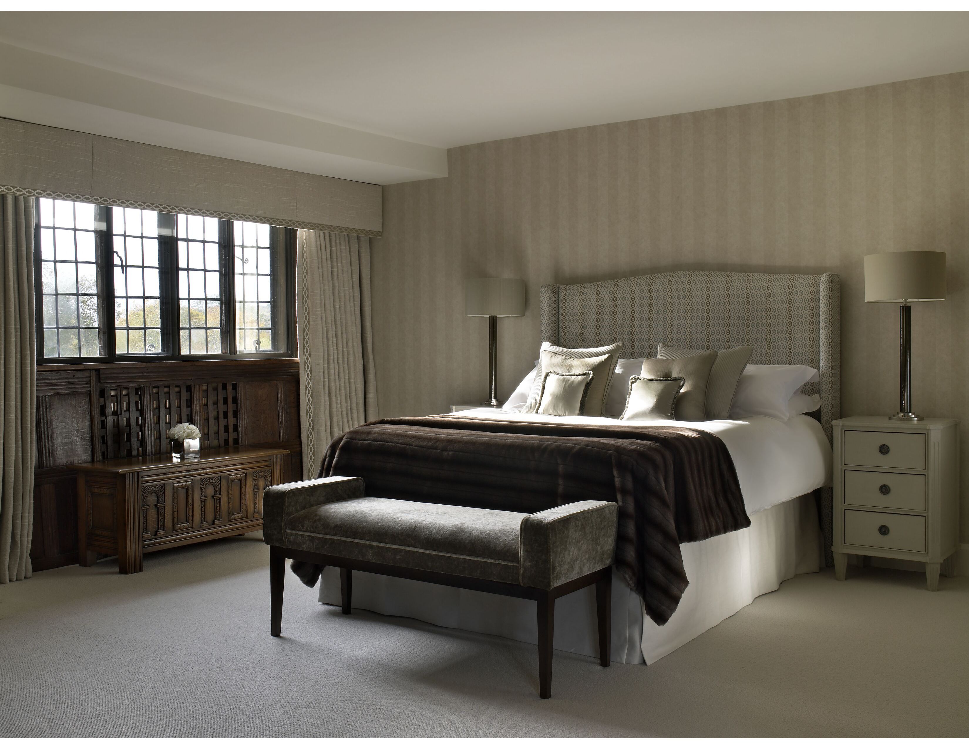 Bedroom scheme with classical bedsides and glass column lamps beside upholstered winged headboard with co-ordinating bed cushions and fur throw.