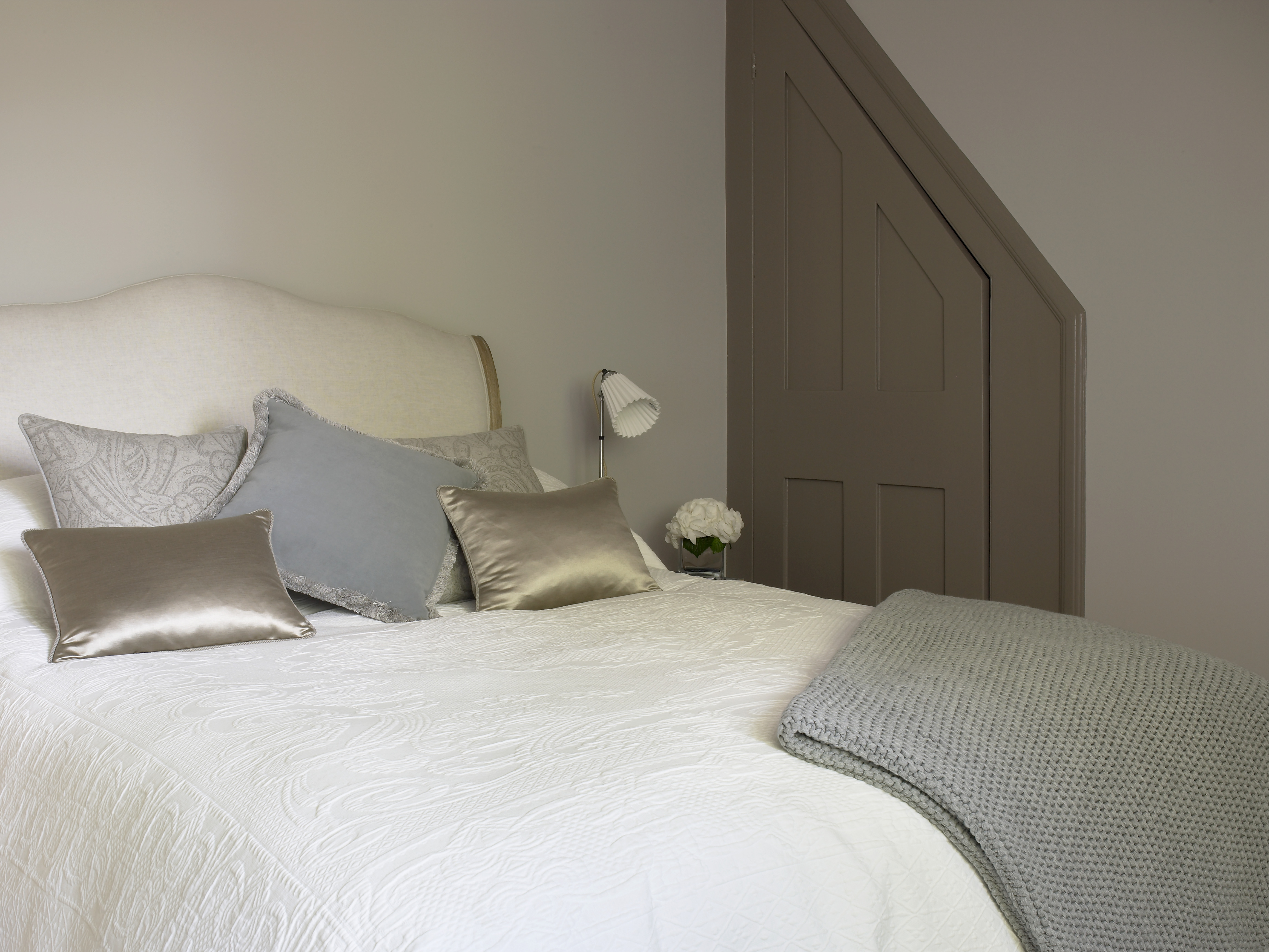 Relaxed guest bedroom scheme with mixed fabric bed cushions and bedside lamp with pleated ceramic shade.