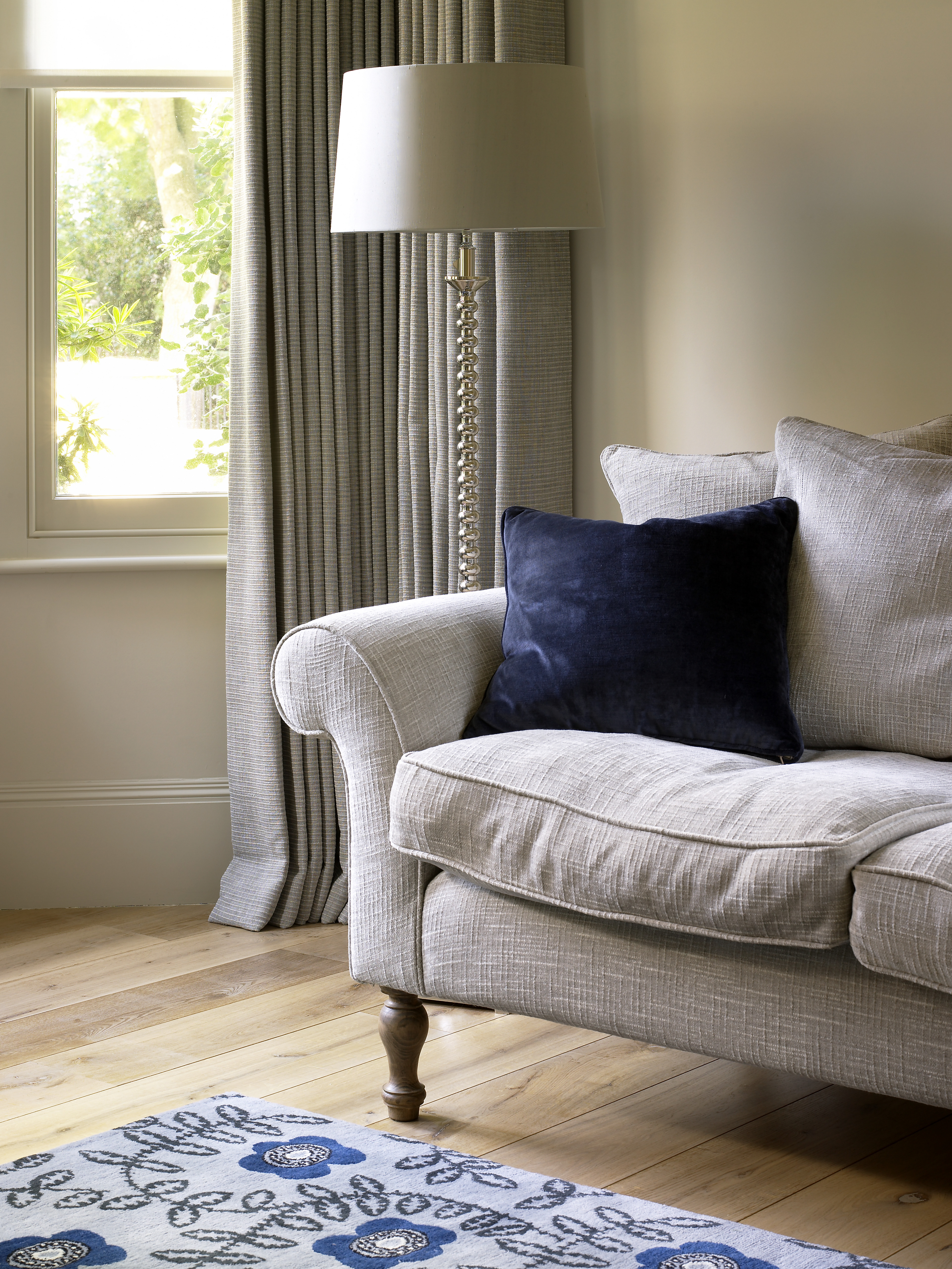 Classical sofa in soft grey linen with blue velvet cushion and Neisha Crosland rug on oak wooden floor.