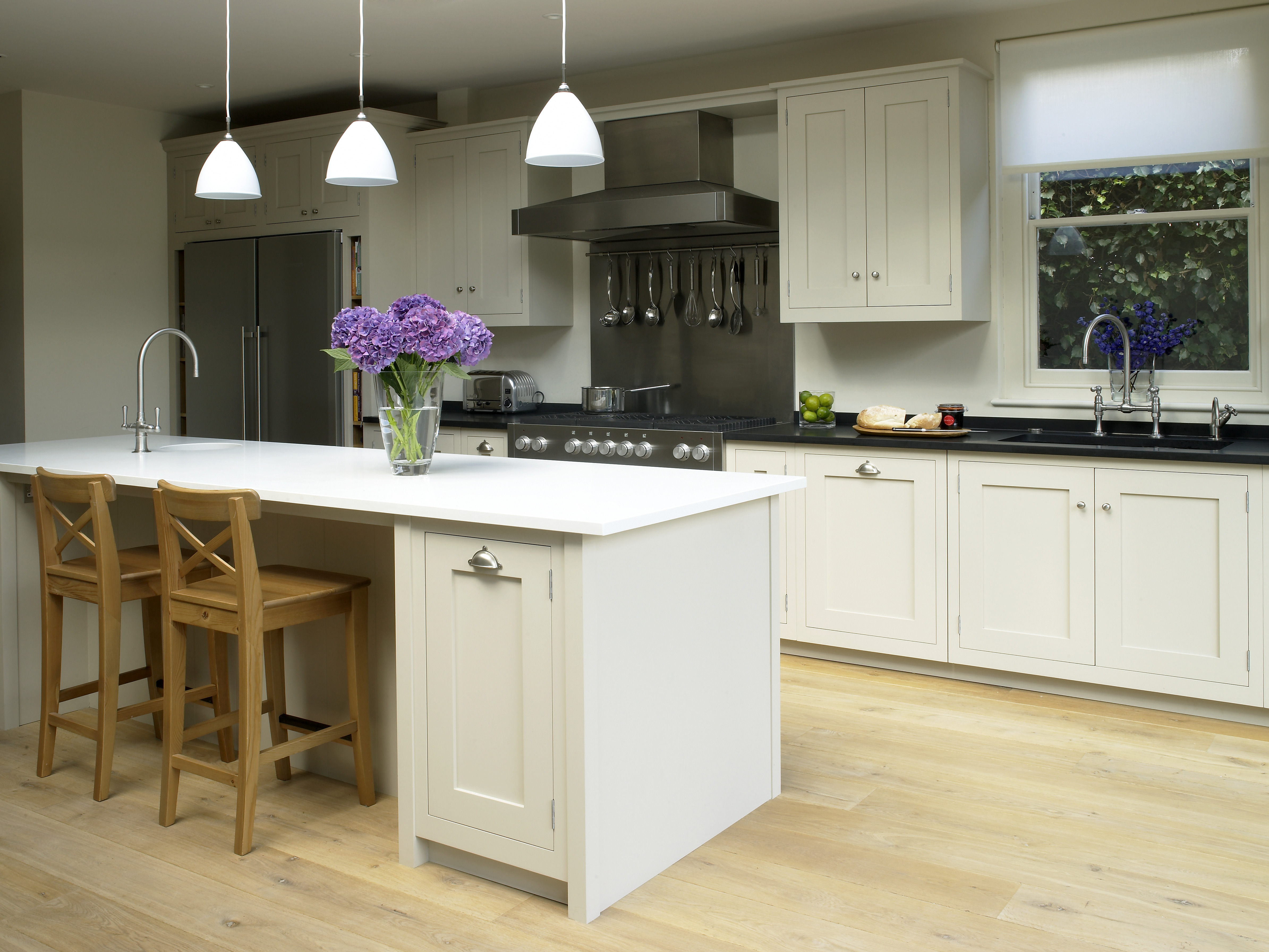 Classic shaker style hand painted wooden kitchen with honed granite worktops and central island with metal pendants.
